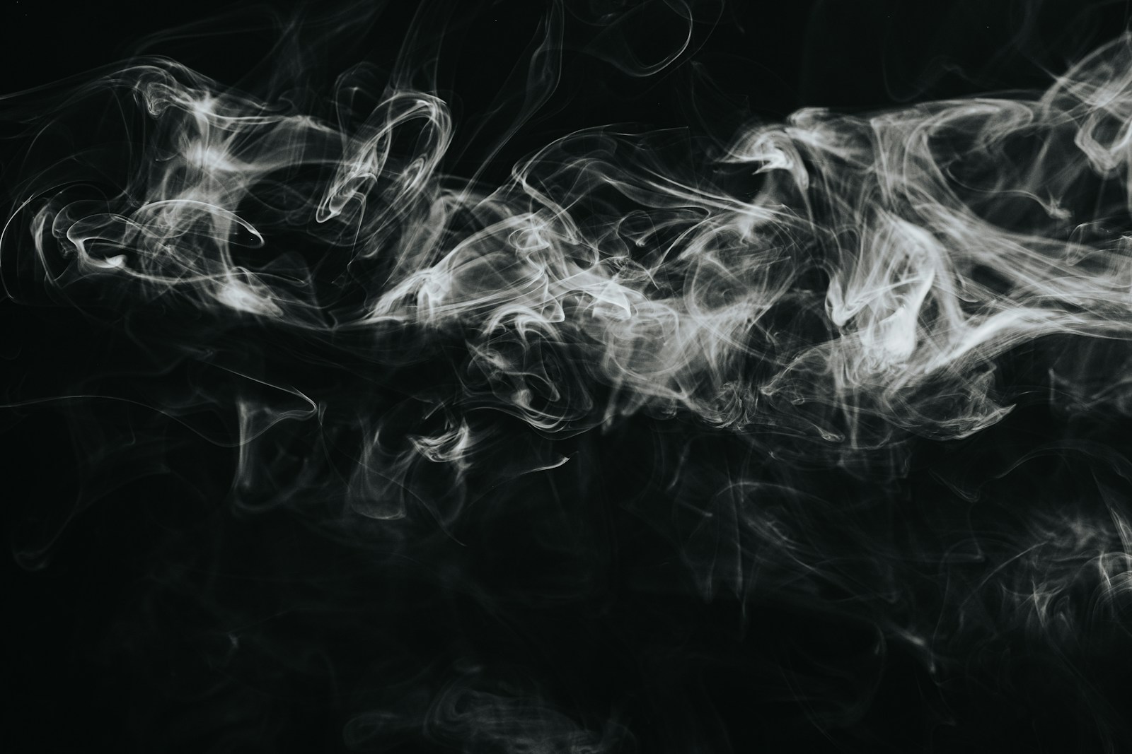 White smoke forming delicate layers and curls against a black background